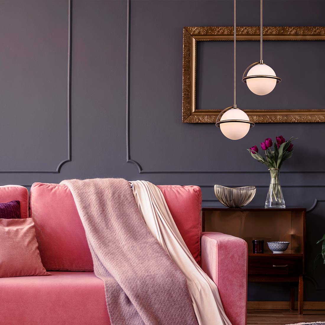 pink couch, with a lighter pink blanket layed across it. In front of a dark purple wall, two gold and opal pendants hanging from the ceiling