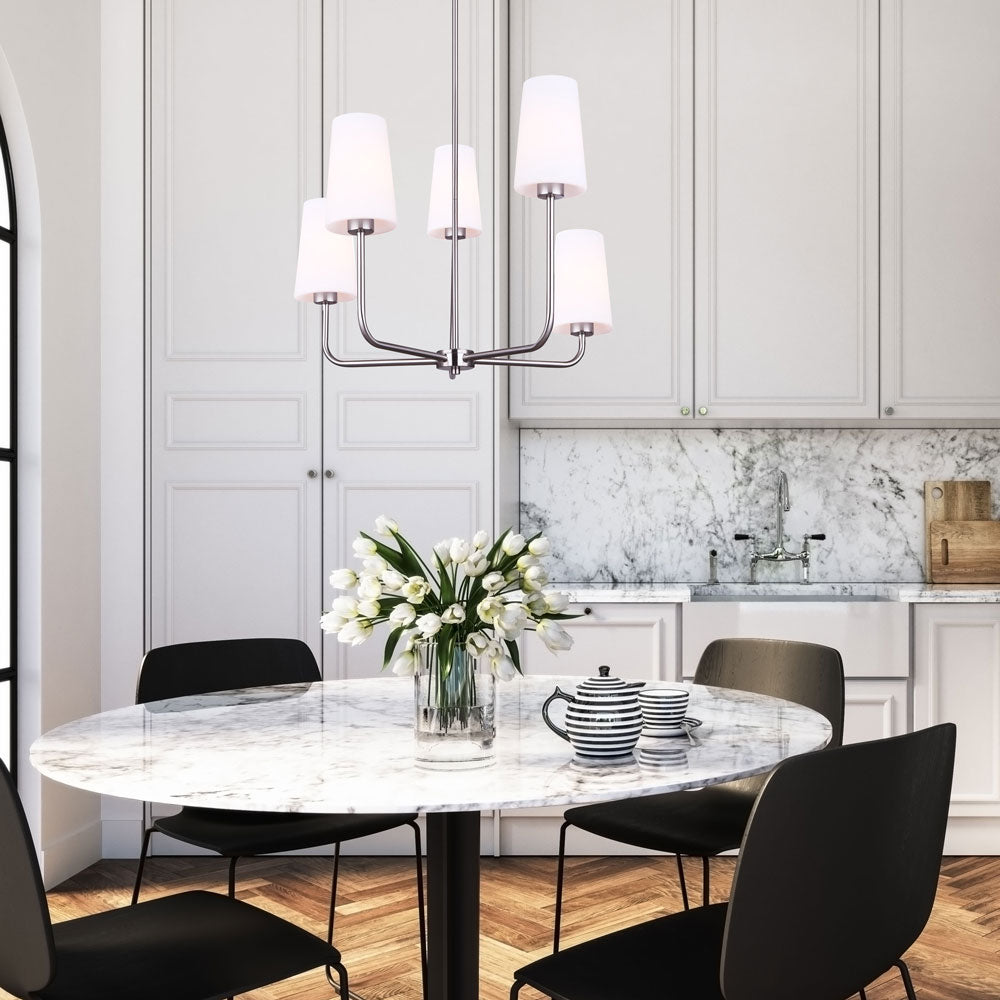 photo of a kitchen with a white tulips on a round table and four black chairs, and light grey cabinets with a photo of a 5 light pendant in a brushed nickel finish and 5 flat opal glass shades hanging in the centre of the room