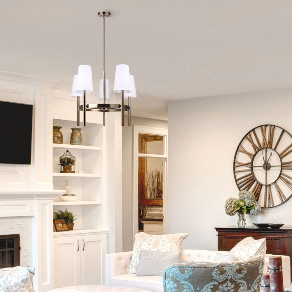 photo of a living room painted white, flat screen tv over the fireplace, white shelf, large wooden clock hung on the wall, white love seat, one turquoirs arm chair, hanging over the seating area is a 5  light chanelier in gold finish with 5 tappered white shades